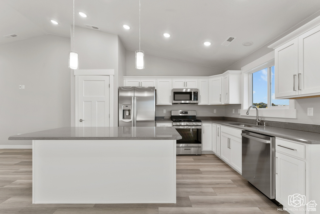 Kitchen with pendant lighting, white cabinets, sink, stainless steel appliances, and a center island