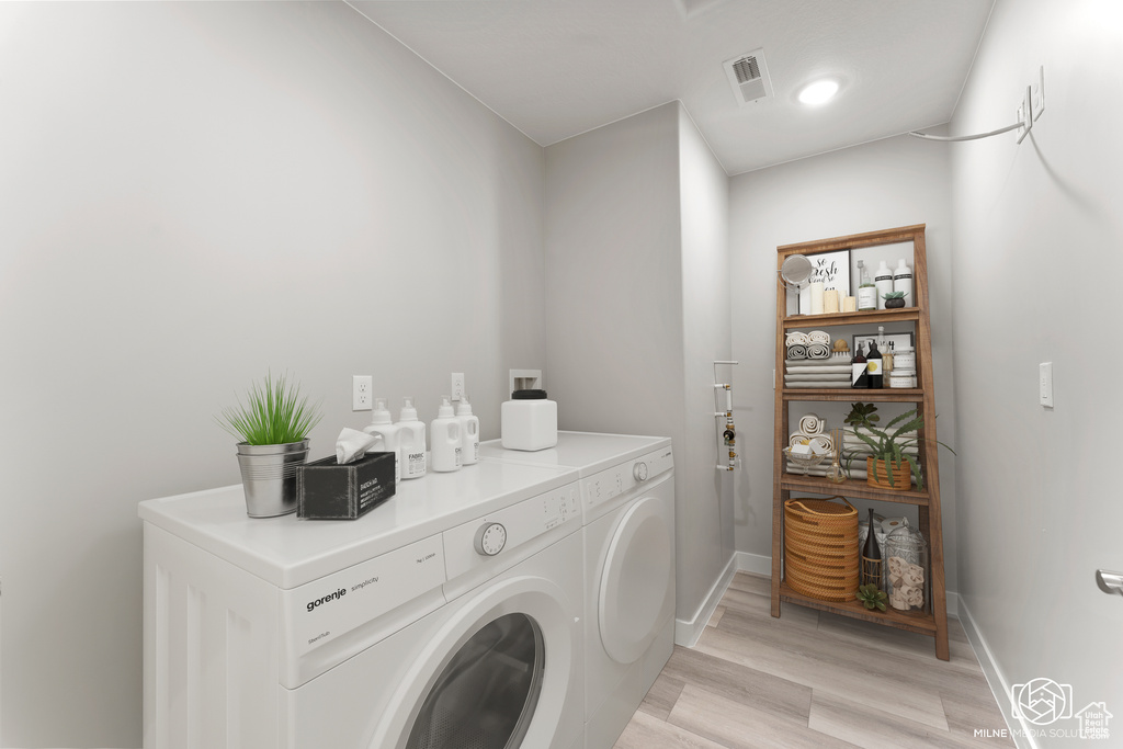 Washroom with washing machine and clothes dryer and light wood-type flooring