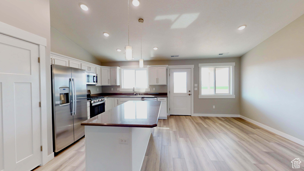 Kitchen featuring a kitchen island, pendant lighting, stainless steel appliances, white cabinetry, and light wood-type flooring