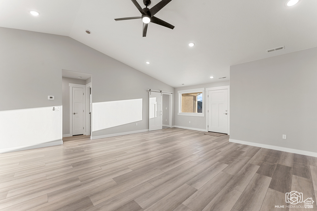 Unfurnished living room featuring ceiling fan, vaulted ceiling, light hardwood / wood-style floors, and a barn door