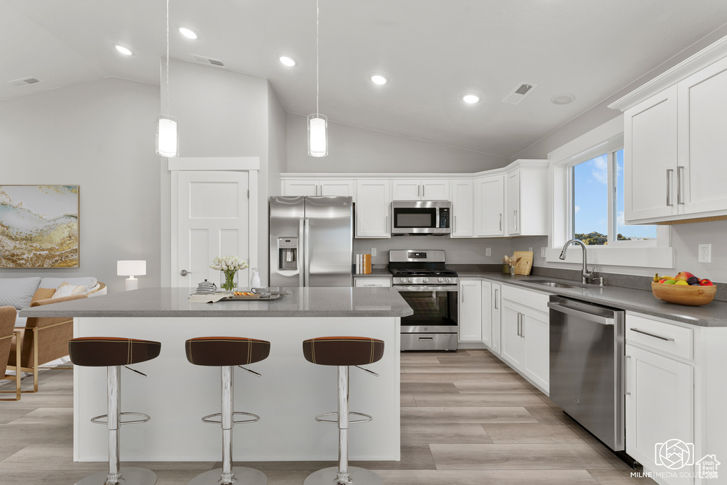 Kitchen featuring hanging light fixtures, sink, white cabinetry, appliances with stainless steel finishes, and a center island