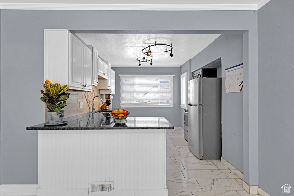 Kitchen with white cabinets, backsplash, stainless steel refrigerator, sink, and kitchen peninsula