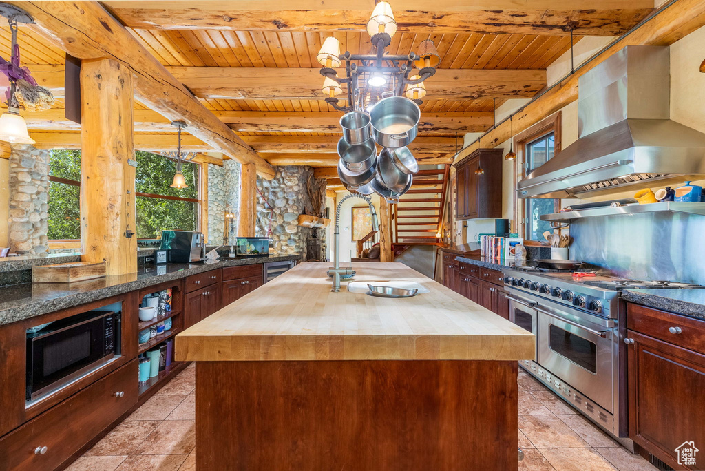 Kitchen featuring ventilation hood, wood counters, black microwave, range with two ovens, and a center island with sink