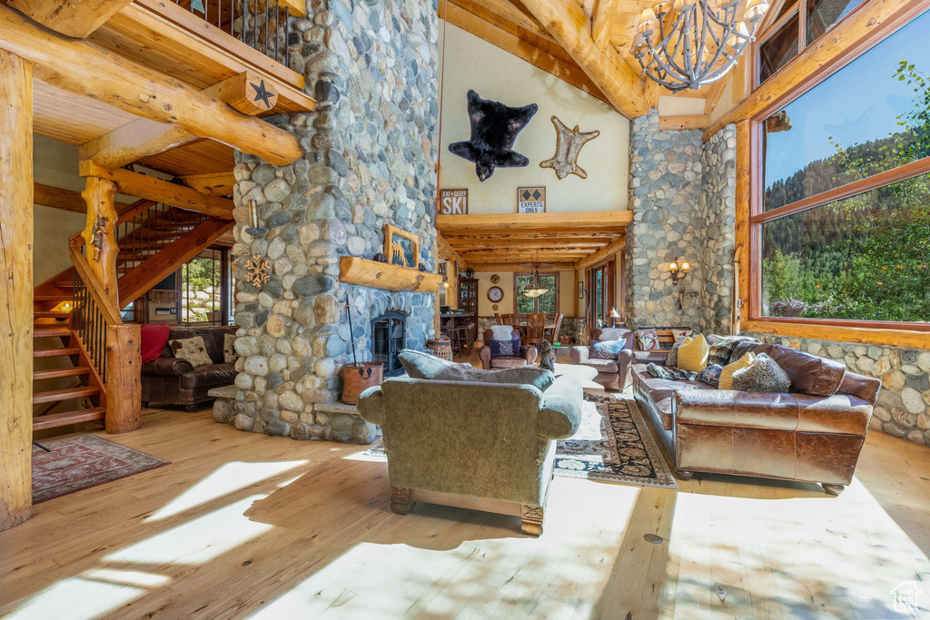Living room with an inviting chandelier, a stone fireplace, hardwood / wood-style floors, beam ceiling, and a towering ceiling