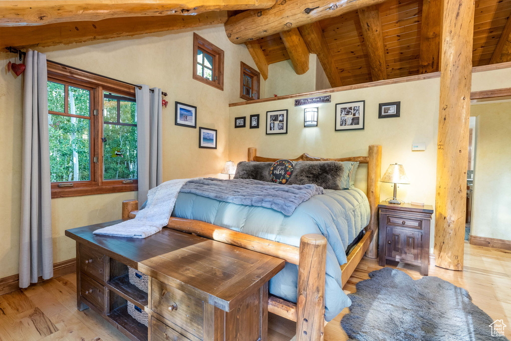 Bedroom with wooden ceiling, lofted ceiling with beams, multiple windows, and light hardwood / wood-style floors