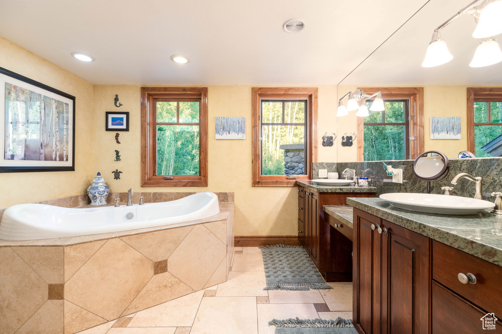 Bathroom with a wealth of natural light, vanity, tiled tub, and tile patterned flooring