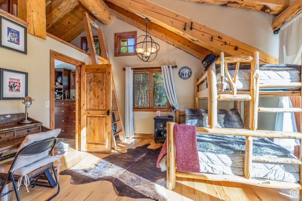 Bedroom with high vaulted ceiling, a wood stove, wood-type flooring, an inviting chandelier, and beam ceiling