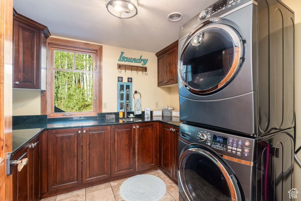 Washroom featuring stacked washer and clothes dryer, cabinets, and light tile patterned flooring