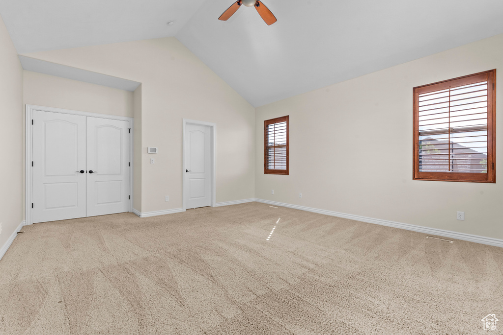 Unfurnished bedroom featuring a closet, ceiling fan, light carpet, and vaulted ceiling