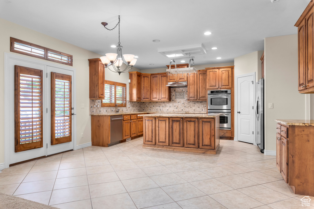 Kitchen with hanging light fixtures, an inviting chandelier, light stone counters, stainless steel appliances, and a kitchen island