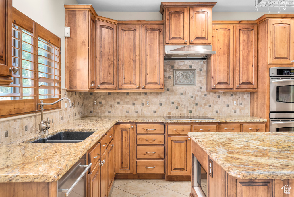 Kitchen with appliances with stainless steel finishes, tasteful backsplash, sink, light stone counters, and light tile patterned flooring