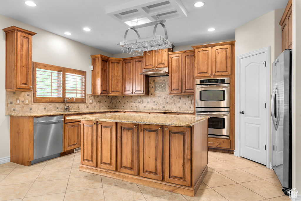 Kitchen with a center island, light stone counters, stainless steel appliances, and decorative backsplash