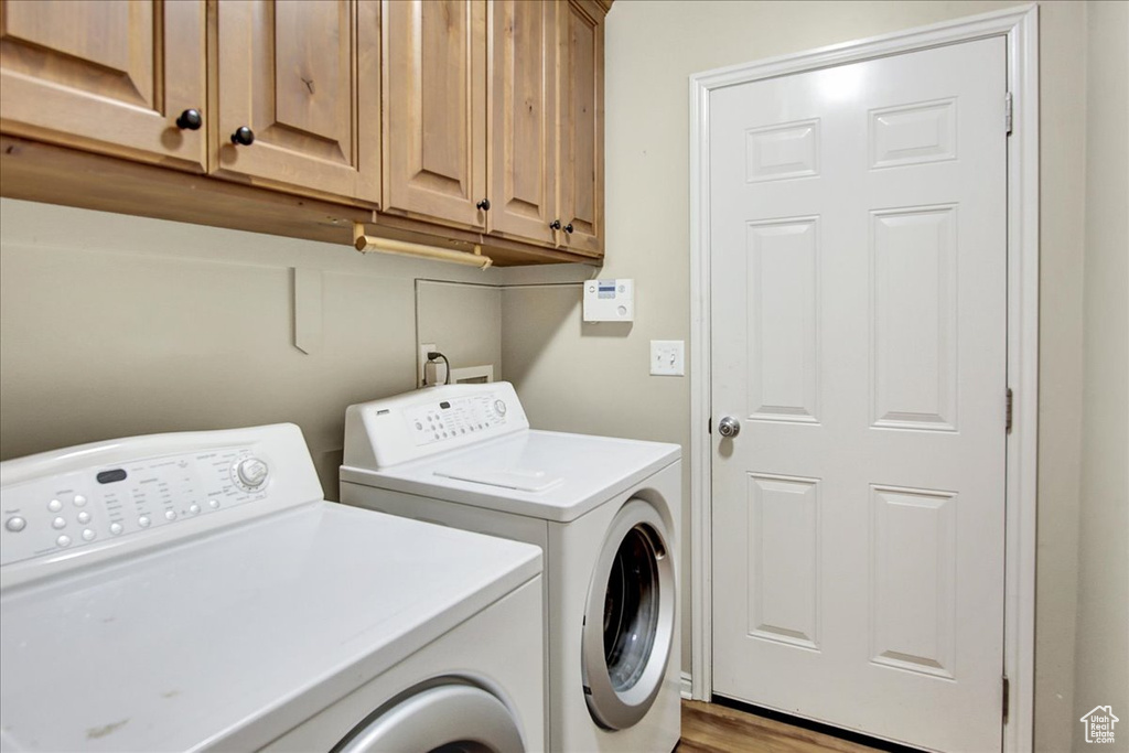 Clothes washing area with cabinets, light hardwood / wood-style floors, and independent washer and dryer