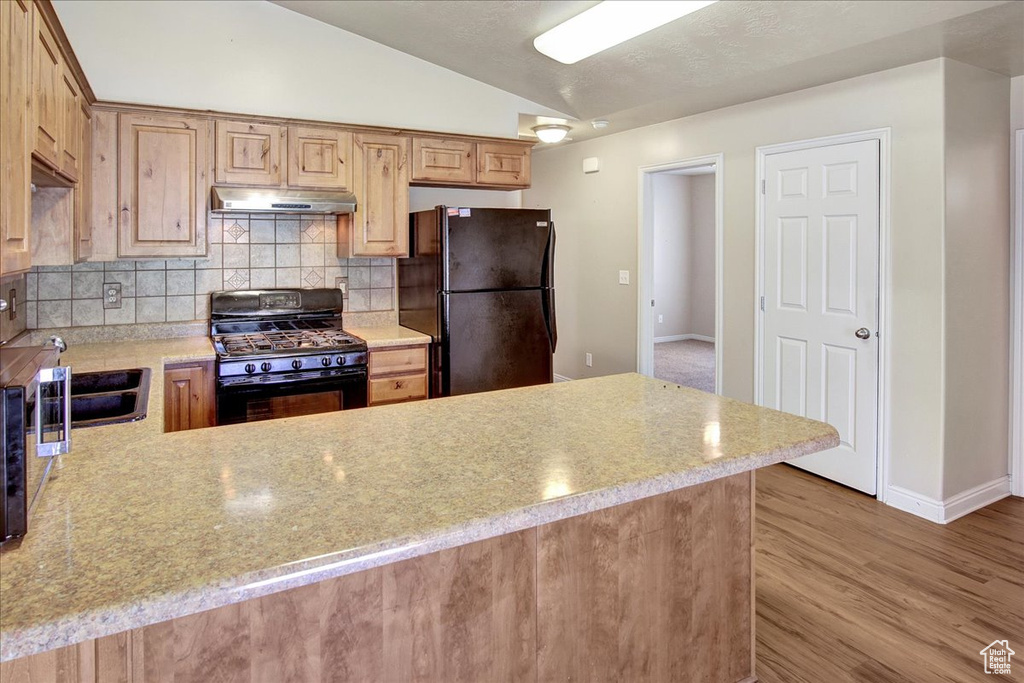 Kitchen featuring black appliances, light hardwood / wood-style floors, kitchen peninsula, decorative backsplash, and lofted ceiling