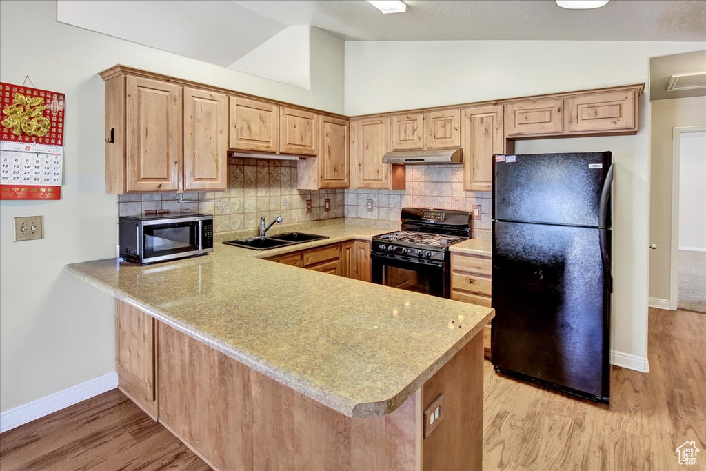 Kitchen with black appliances, light hardwood / wood-style floors, kitchen peninsula, sink, and lofted ceiling