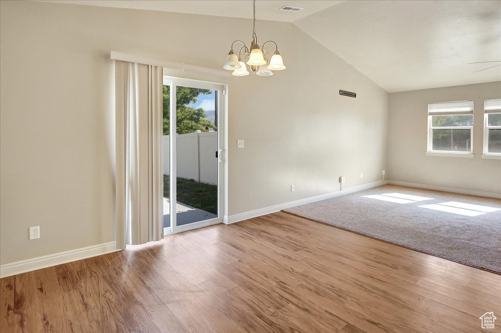 Unfurnished room featuring lofted ceiling, a healthy amount of sunlight, a chandelier, and light hardwood / wood-style floors