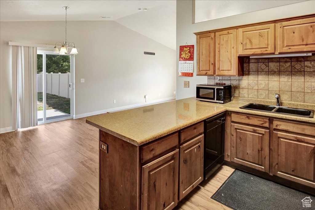 Kitchen with a notable chandelier, kitchen peninsula, sink, vaulted ceiling, and light hardwood / wood-style floors
