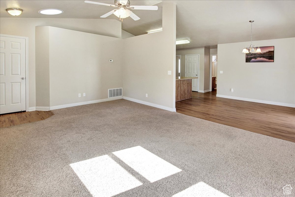 Empty room featuring ceiling fan with notable chandelier, lofted ceiling, and hardwood / wood-style flooring