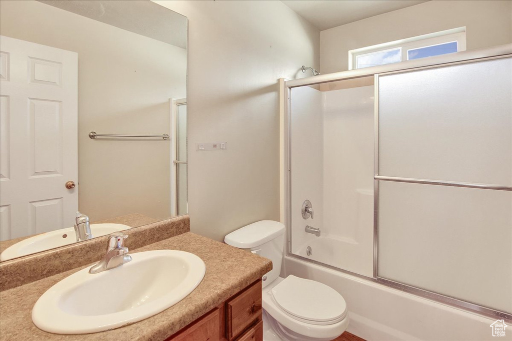 Full bathroom with toilet, bath / shower combo with glass door, and vanity