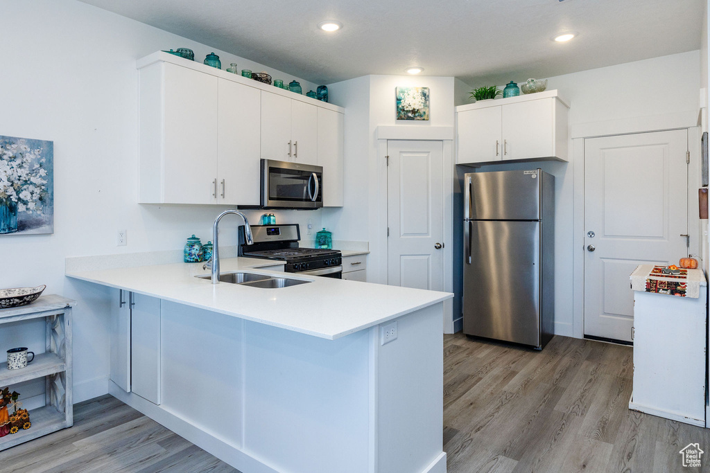 Kitchen featuring appliances with stainless steel finishes, white cabinetry, light hardwood / wood-style floors, and kitchen peninsula