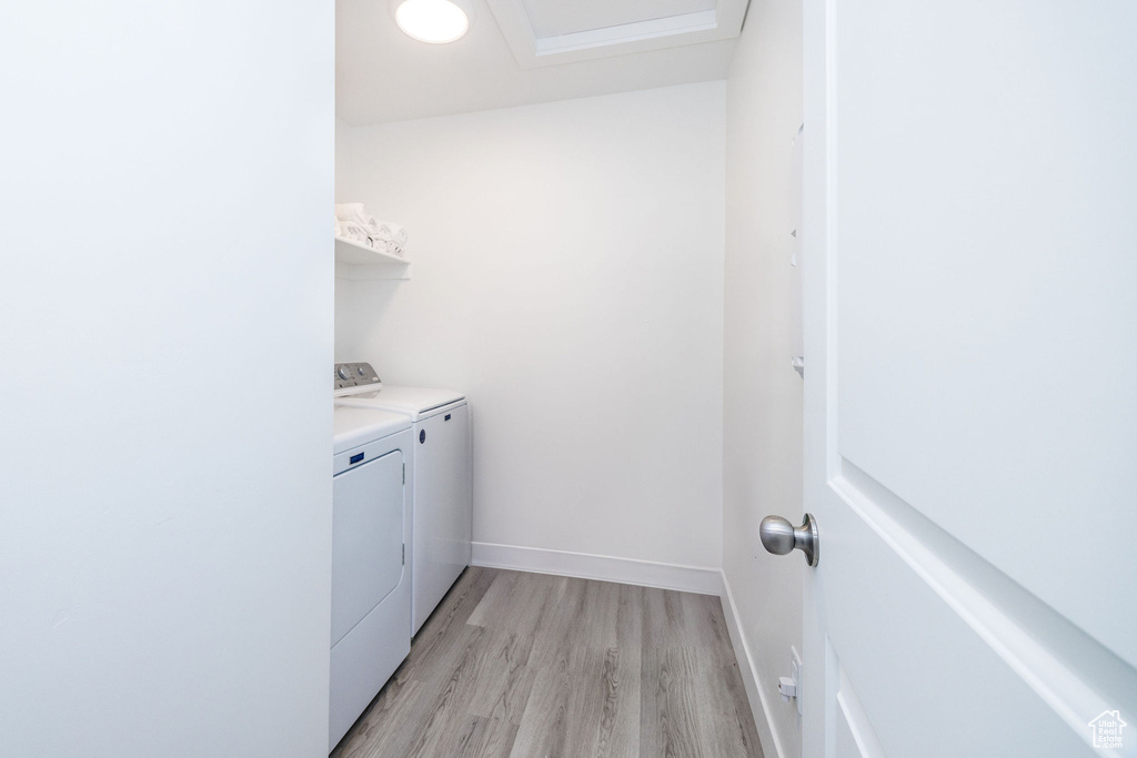 Clothes washing area with independent washer and dryer and light hardwood / wood-style flooring