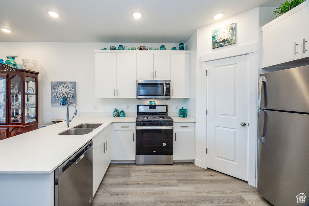 Kitchen featuring appliances with stainless steel finishes, white cabinetry, kitchen peninsula, and sink