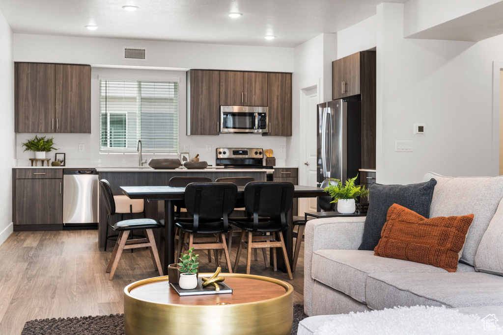 Kitchen with appliances with stainless steel finishes, dark brown cabinets, a breakfast bar area, and light hardwood / wood-style floors