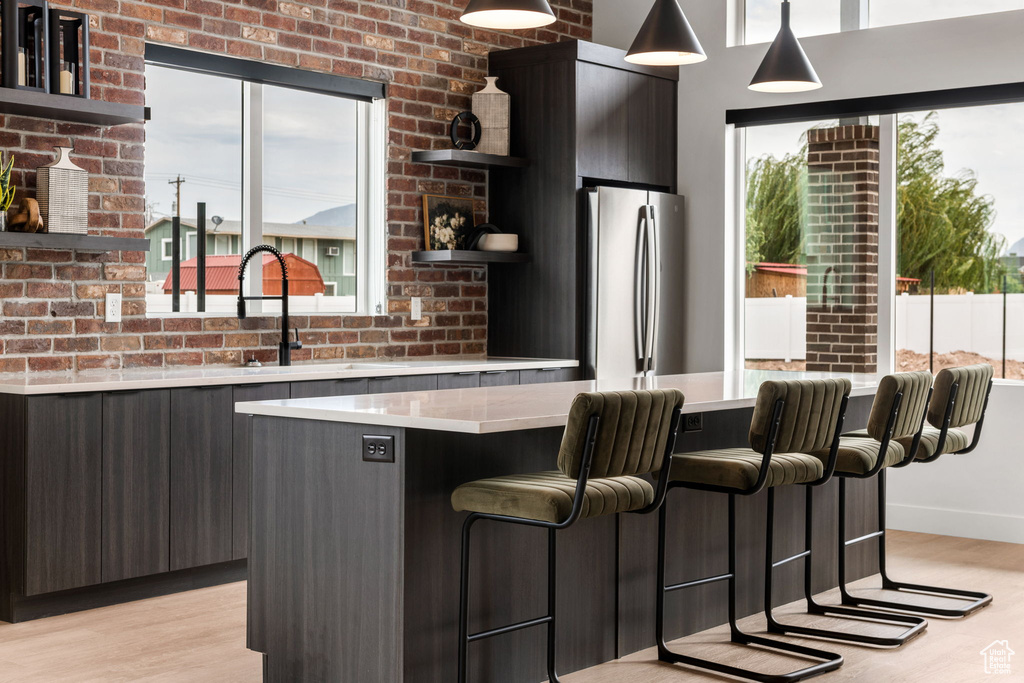 Bar with pendant lighting, stainless steel fridge, light hardwood / wood-style flooring, sink, and brick wall