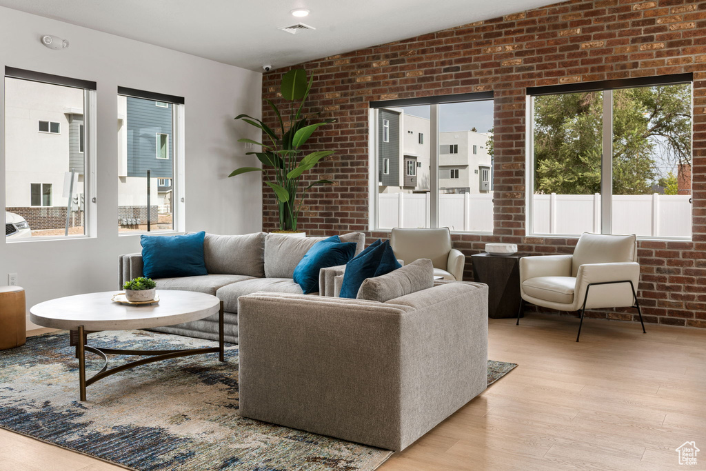 Living room with light wood-type flooring, vaulted ceiling, plenty of natural light, and brick wall