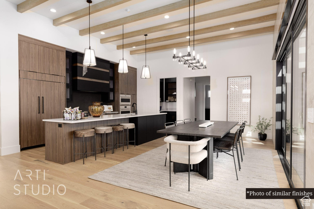 Kitchen with beamed ceiling, light hardwood / wood-style floors, a kitchen bar, hanging light fixtures, and a kitchen island with sink