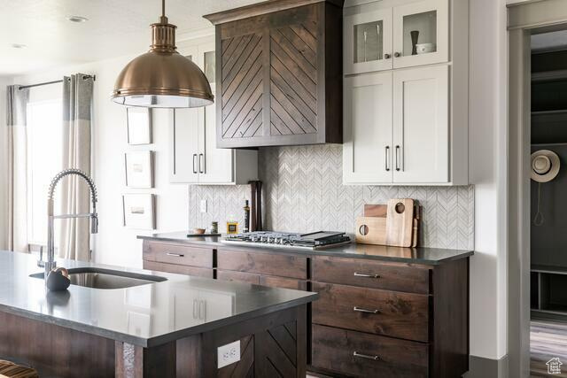 Kitchen with stainless steel gas stovetop, dark brown cabinets, white cabinetry, and sink