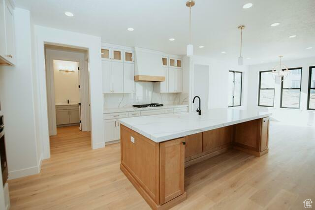 Kitchen featuring pendant lighting, a large island with sink, white cabinets, custom exhaust hood, and light stone countertops