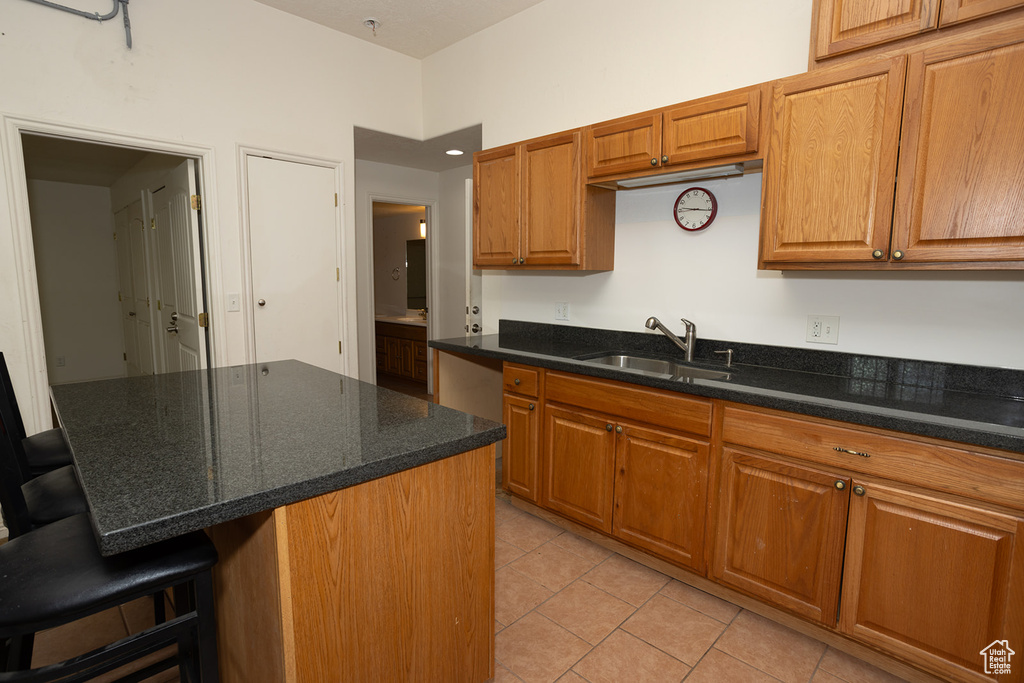 Kitchen with a kitchen island, a breakfast bar area, light tile patterned floors, sink, and dark stone counters