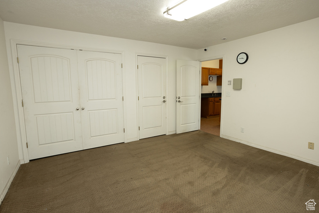 Unfurnished bedroom with dark carpet, multiple closets, and a textured ceiling