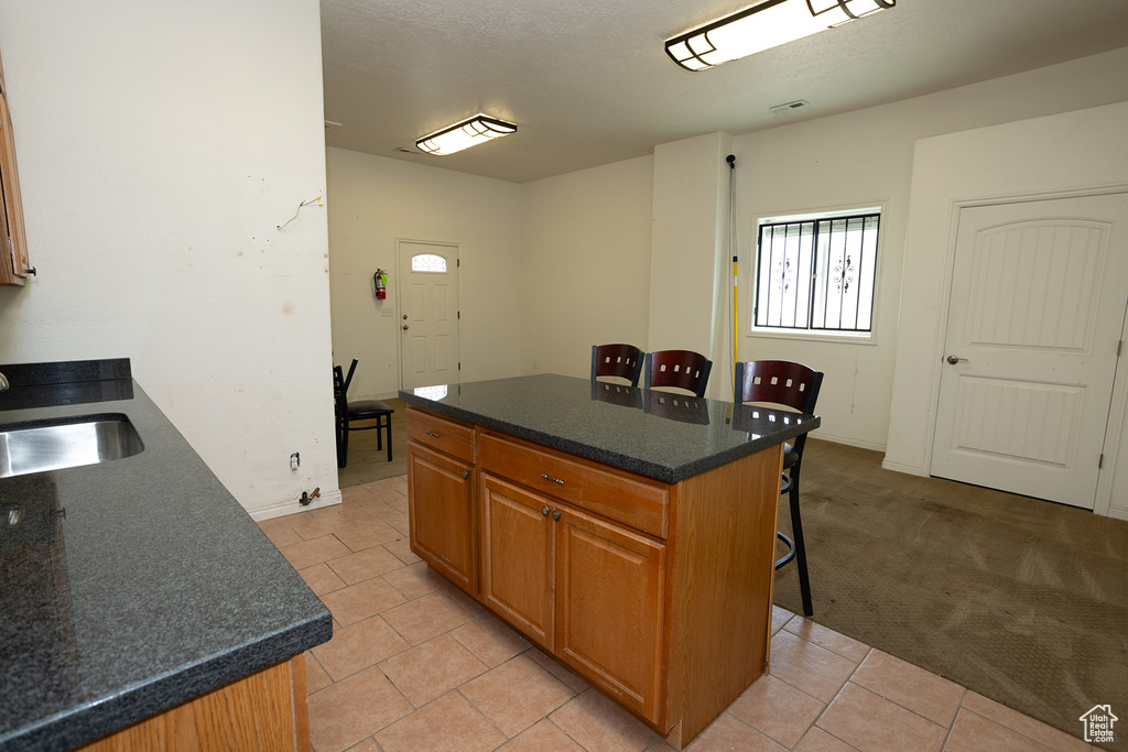 Kitchen featuring a center island, light colored carpet, sink, a kitchen bar, and a textured ceiling
