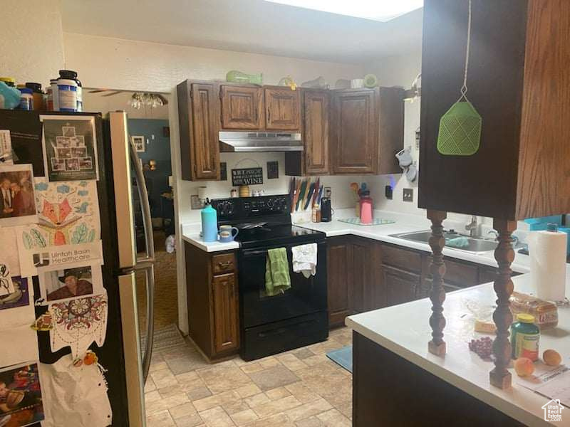 Kitchen with black electric range, stainless steel refrigerator, sink, and dark brown cabinets