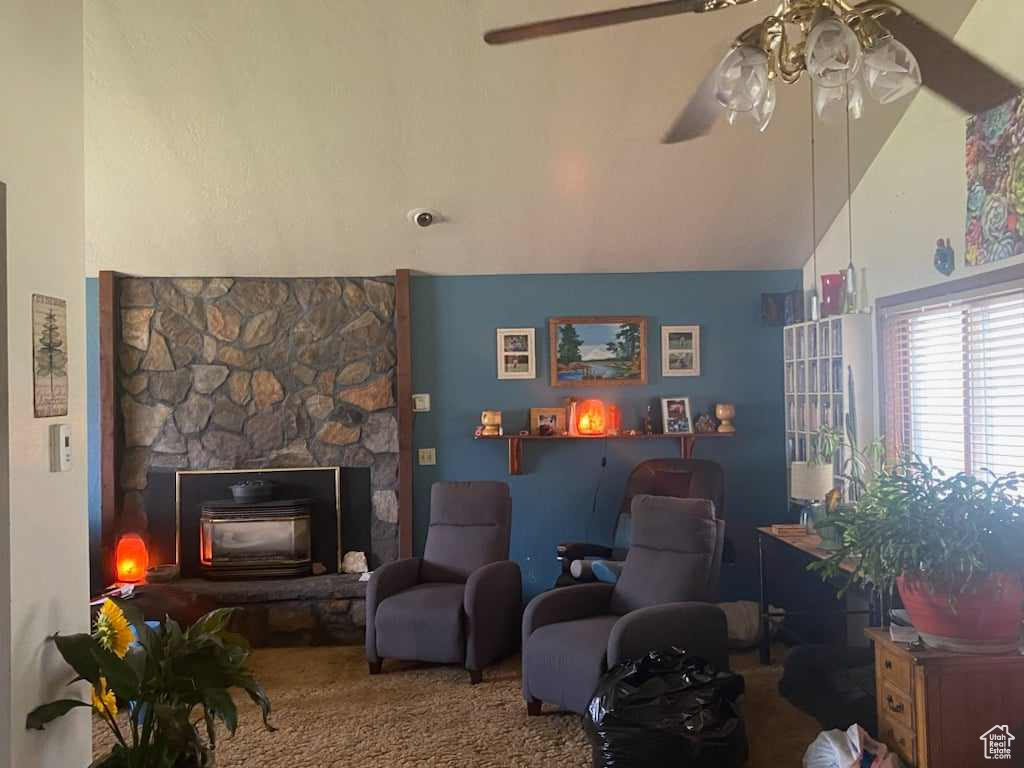 Carpeted living room with ceiling fan, a stone fireplace, and high vaulted ceiling