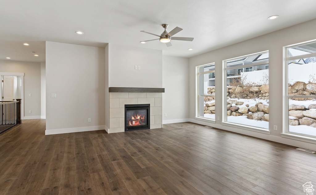 Unfurnished living room with a fireplace, plenty of natural light, ceiling fan, and dark wood-type flooring