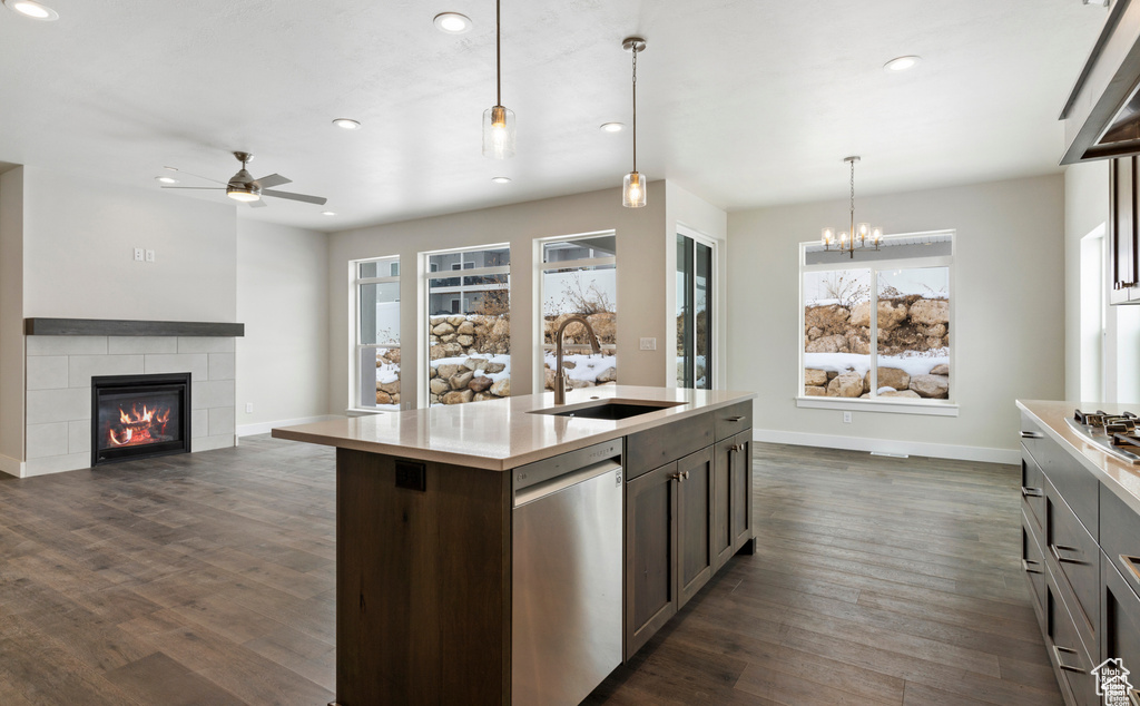 Kitchen featuring ceiling fan with notable chandelier, a tile fireplace, an island with sink, sink, and dark wood-type flooring