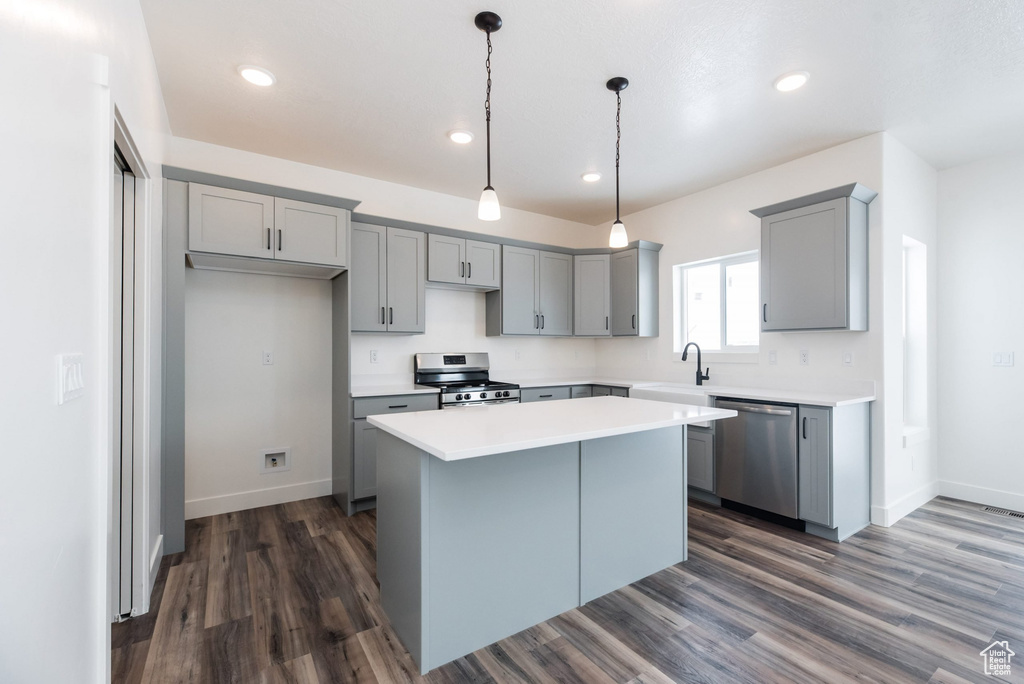 Kitchen with gray cabinetry, hanging light fixtures, a center island, stainless steel appliances, and dark wood-type flooring