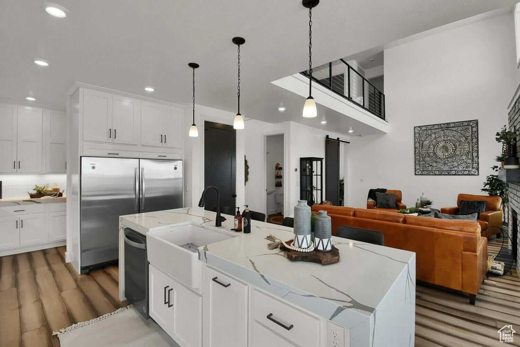 Kitchen with light wood-type flooring, white cabinetry, an island with sink, light stone countertops, and appliances with stainless steel finishes