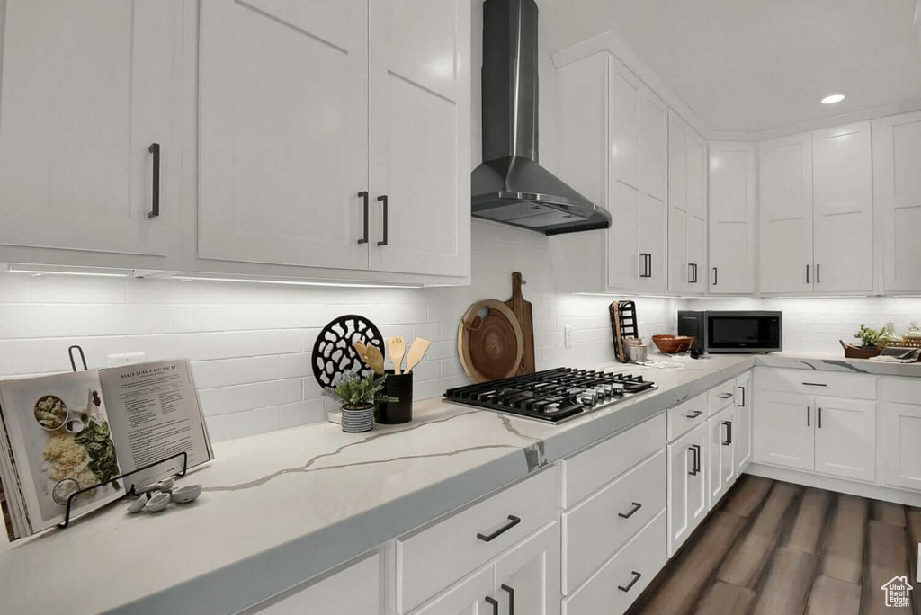 Kitchen with white cabinets, light stone counters, stainless steel appliances, wall chimney range hood, and dark hardwood / wood-style floors