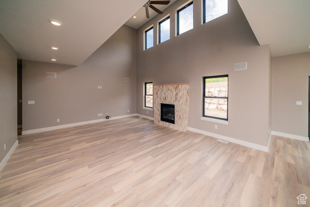 Unfurnished living room featuring a high ceiling, ceiling fan, and light hardwood / wood-style flooring