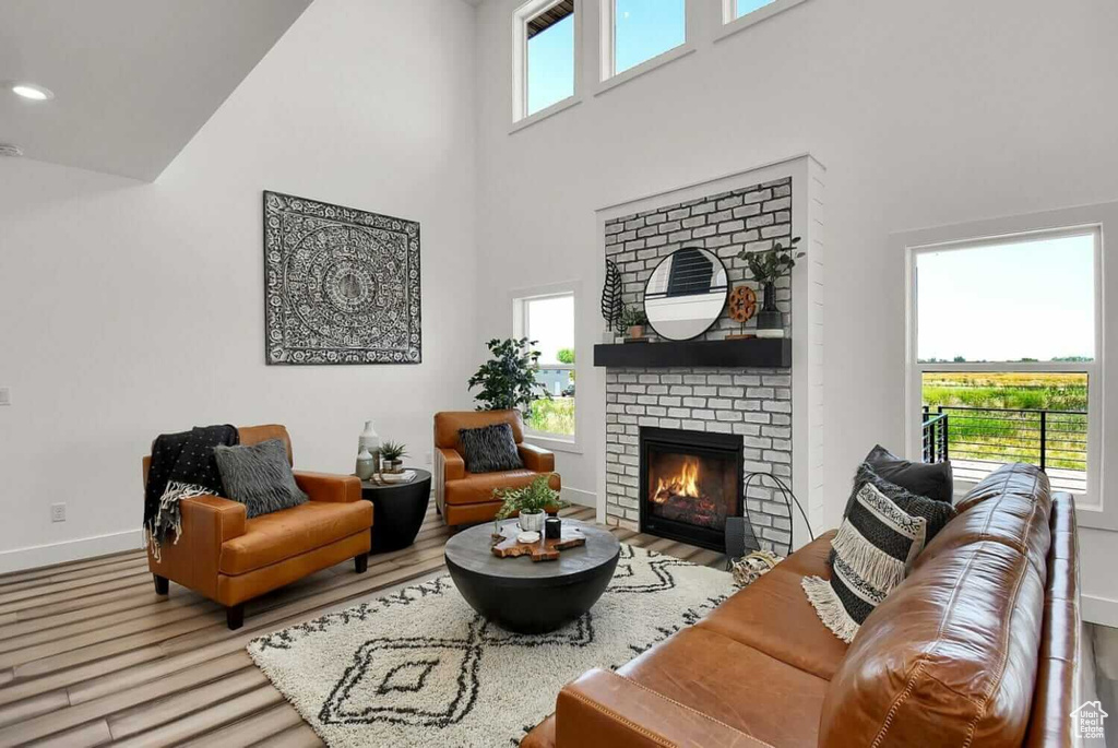 Living room featuring a towering ceiling, light hardwood / wood-style floors, and a brick fireplace