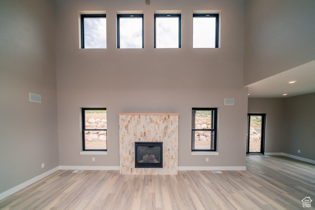 Unfurnished living room with a high ceiling, a tile fireplace, plenty of natural light, and light hardwood / wood-style flooring