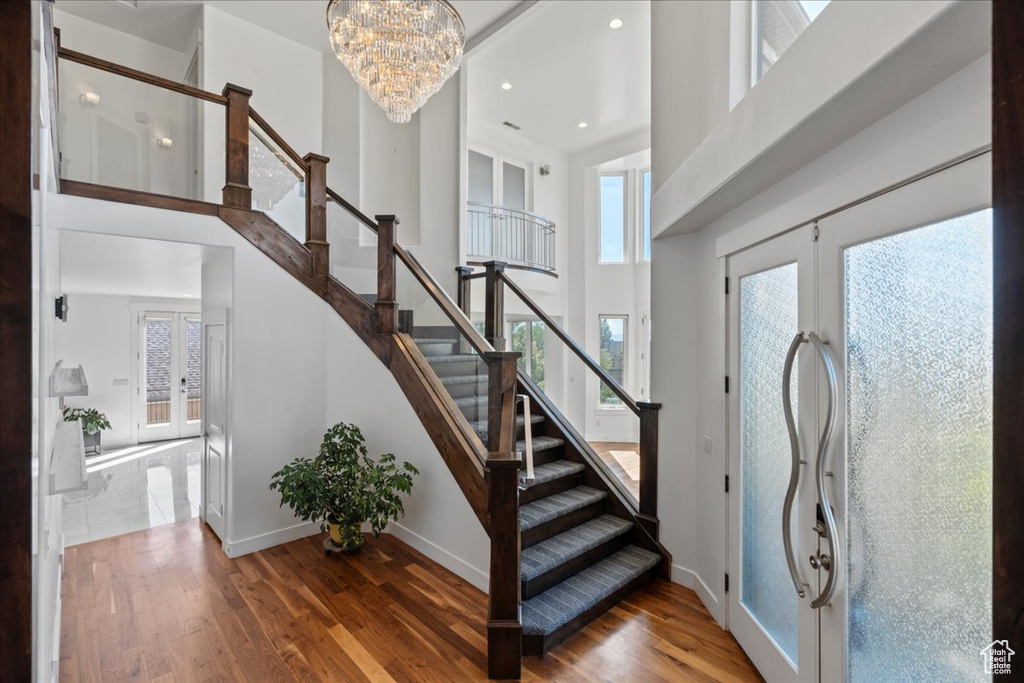 Stairs with wood-type flooring, an inviting chandelier, plenty of natural light, and french doors