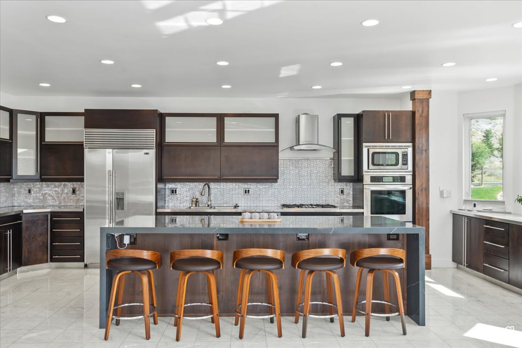 Kitchen featuring built in appliances, a breakfast bar, a center island, and wall chimney range hood