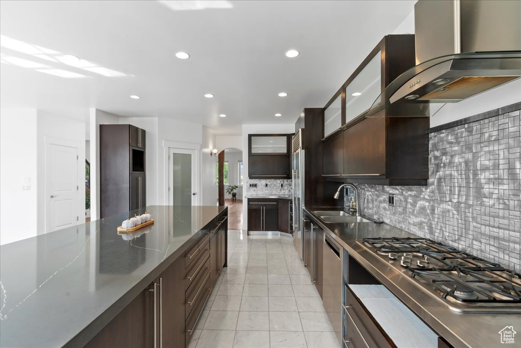 Kitchen featuring wall chimney range hood, sink, decorative backsplash, appliances with stainless steel finishes, and dark brown cabinetry