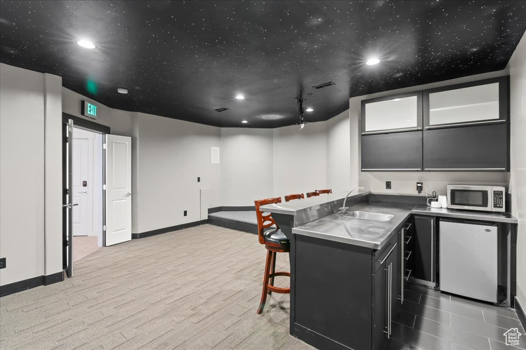 Kitchen with light colored carpet, fridge, sink, kitchen peninsula, and a breakfast bar area