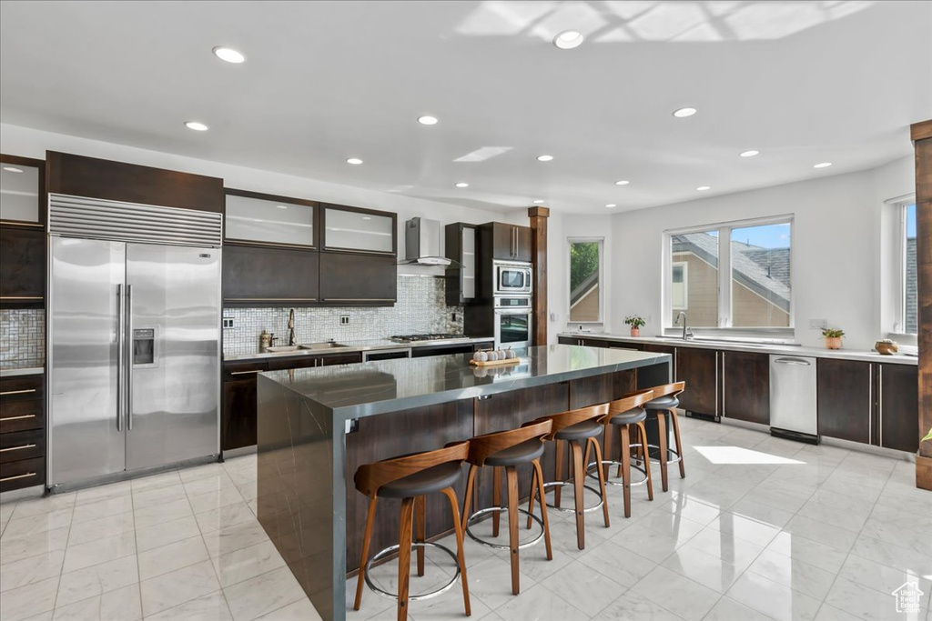 Kitchen featuring backsplash, a center island, sink, wall chimney exhaust hood, and built in appliances